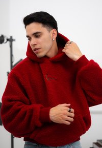 Κόκκινη φλις ζακέτα με μεγάλο καπέλο, πλεκτές μανσέτες και μπροστινή τσέπη. Διαθέτει υφή και ένα μικρό κεντημένο λογότυπο.