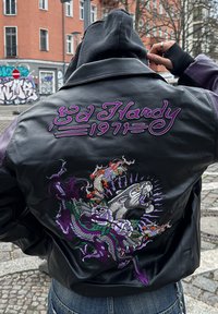 Veste en cuir noir avec du texte brodé violet "Ed Hardy 1971" et des motifs complexes de dragon et d'un animal parmi des fleurs.