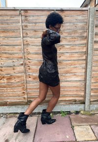 Juoda mini suknelė dekoruota blizgančiomis juodomis akutėmis, ilgomis rankovėmis, aptempta silueto ir tekstūruoto blizgesio. Derinama su laisvais juodais aulinukais.