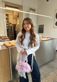 Cardigan grigio chiaro con collo arricciato, jeans a gamba larga blu scuro e borsa lavanda arricciata, sullo sfondo di una panetteria.