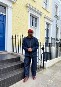 Jachetă și pantaloni din denim albastru închis, guler maro, asortați cu o căciulă tricotată roșie și pantofi maro, stând pe trepte cu plăci negre.