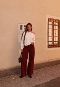 Off-white, oversized trui met losse mouwen, gecombineerd met bordeaux wijde broekspijpen. Zwarte schoenen met hak en een kleine zwarte handtas.