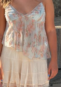 Blommönstrad, lätt topp med ett flödande design i pastellfärger; kombinerad med en lagd, krämfärgad kjol med volanger och spetskant.