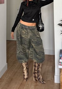 Personne portant une veste courte noire Adidas, un pantalon ample camouflage, et des bottes montantes à motif peau de serpent à l'intérieur.