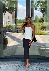 Αμάνικη λευκή μπλούζα συνδυασμένη με μία μαύρη εφαρμοστή μίντι φούστα. Τα αξεσουάρ περιλαμβάνουν ένα χρυσό βραχιόλι και γόβες με λεοπάρ σχέδιο. Διαφανές γυάλινο φόντο.