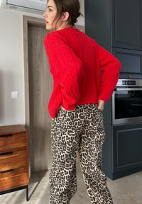 Κόκκινο πουλόβερ με πλέξη καλωδίων και ρίγες στο στρίφωμα, σε συνδυασμό με παντελόνι ευρείας γραμμής με σχέδιο λεοπάρ, που διαθέτει τσέπες και άνετη εφαρμογή.