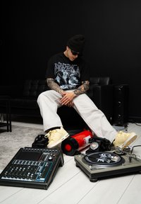 Černé grafické tričko s textem "FAVELA", krémové široké kalhoty, žluté tenisky, gramofon, mixážní pult, vintage telefon, hasicí přístroj.