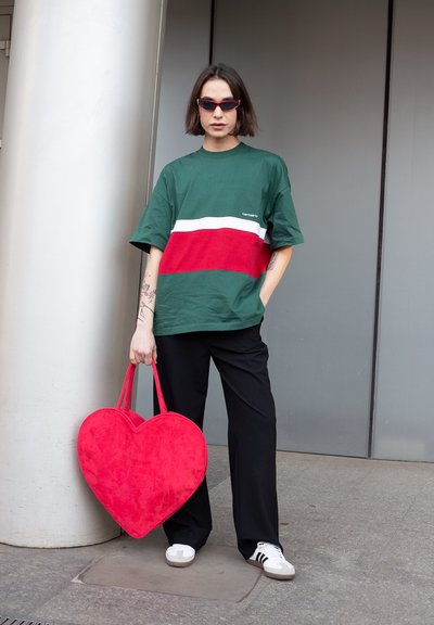 Camiseta a rayas verde y roja, pantalones negros, bolso rojo en forma de corazón y zapatillas blancas con rayas negras. Textura de tela suave.