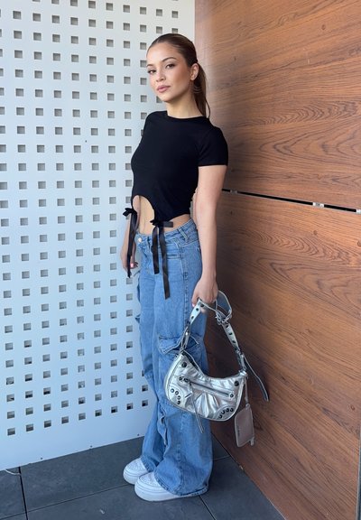 Top corto negro con lazos laterales, jeans baggy azul claro y un bolso metálico plateado con detalles en hardware. Texturas suaves, diseño hasta el muslo.