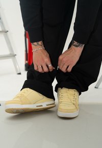 Sneaker gialli con mesh testurizzato e pannelli in pelle solidi; presentano lacci e suole bianche; indossati con pantaloni neri.