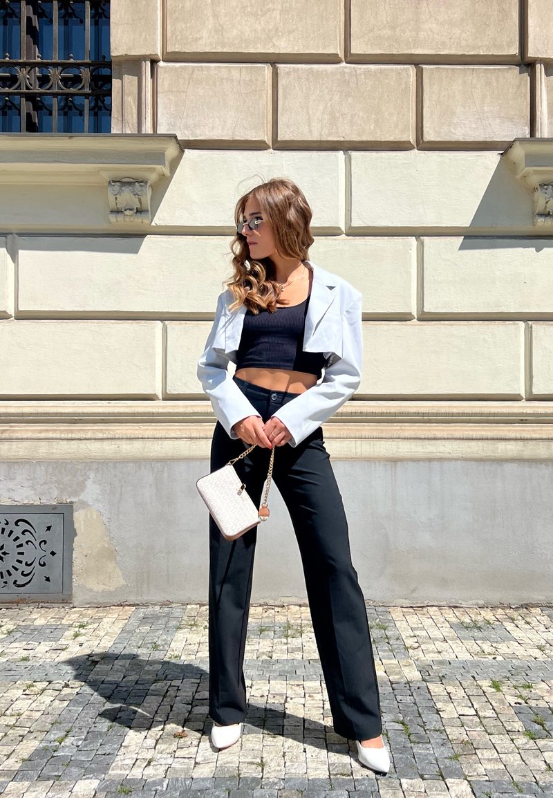 Λευκό κομμένο σακάκι, μαύρο crop top, μαύρο ταγέρ παντελόνι, άσπρα στιλέτο με μυτερή μύτη και μια μικρή άσπρη τσάντα με χρυσή αλυσίδα.