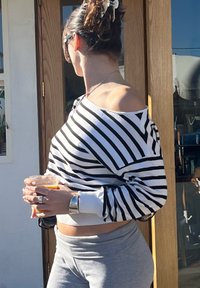 Csíkos, vállakat szabadon hagyó pulóver fekete-fehér színben, szürke melegítőnadrággal párosítva. Egy személy átlátszó poharat tart, benne narancssárga itallal.