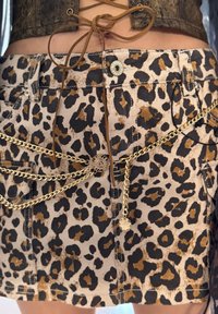 Δημοφιλές τζιν φούστα με στάμπα λεοπάρ, που διαθέτει φραγμένο στρίφωμα, κούμπωμα με μεταλλικό κουμπί και χρυσές αλυσίδες με υφή.