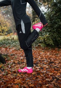 Černý sportovní dlouhý rukáv s šedými detaily; černé kalhoty s síťovanou texturou; jasně růžové běžecké boty s bílými pruhy.