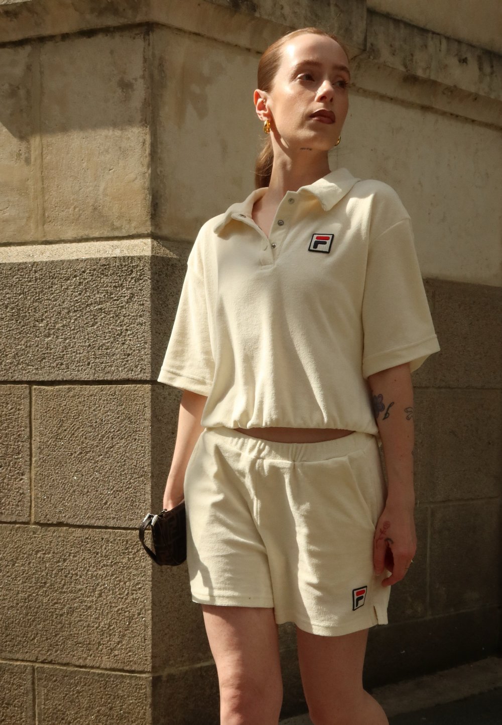 Polo shirt beige, à texture douce, avec des manches courtes et un col, assorti à un short. Présente un petit logo sur la poitrine.