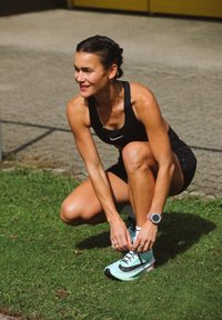 Nike športni copati z zasnovo v mint zeleni in črni barvi. Posameznik nosi črn športni komplet in si prilagaja vezalke na čevljih.