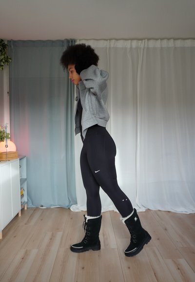 Leggings negras, sudadera gris con cremallera y botas negras forradas de piel. Tela texturizada, diseño elegante, logo minimalista de Nike en los leggings.