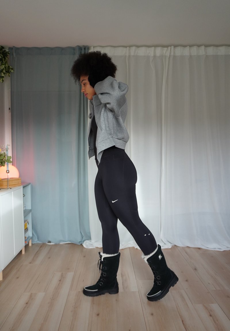 Leggings neri, felpa grigia con zip e stivali neri foderati in pelliccia. Tessuto testurizzato, design elegante, logo Nike minimale sulle leggings.