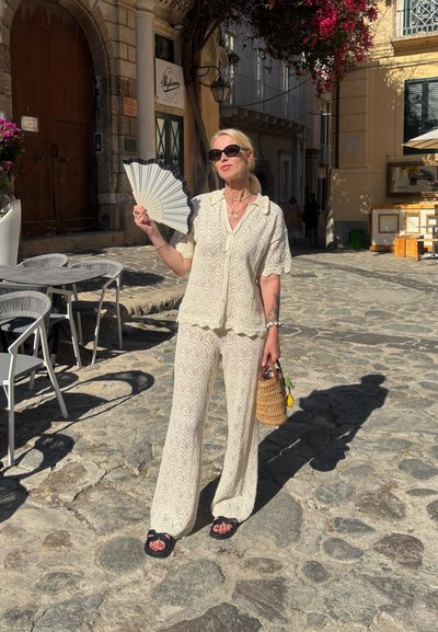 Conjunto de dos piezas de color claro y textura, con un ajuste holgado; adornado con un patrón. Accesorios incluyen un bolso de mimbre y un abanico blanco.