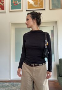 Crna majica s dugim rukavima, u kontrastu s bež hlačama širokih nogavica. Outfit uključuje crnu torbu s pletenom ručkom i srebrnim detaljima.