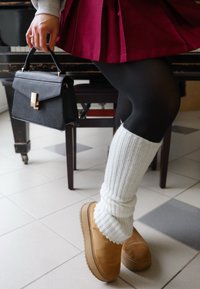 Stivaletti alla caviglia in suede beige, calze a coste bianche fino al ginocchio, collant neri e una gonna plissettata bordeaux. Viene tenuta una borsa nera con dettagli in oro.