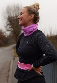 Haut noir à manches longues avec motif à pois, tour de cou rose et sac banane rose assorti. Tissu lisse, coupe sportive, cadre extérieur.