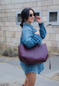 Vīna krāsas ādas tote soma ar strukturētu dizainu un īsām rokturiem, kombinēta ar džinsa krekla kleitu un apaļām saulesbrillēm.