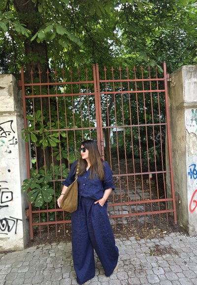 Conjunto de dos piezas de lino en azul marino oscuro, que incluye una camisa de botones y pantalones de pierna ancha. Bolsa de hombro marrón y gafas de sol oscuras, de pie junto a una puerta roja.