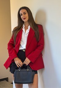 Rød oversized blazer over en hvit skjorte, parret med svarte shorts. Holder en liten svart håndveske med gullakenter og har på seg flere ringer.