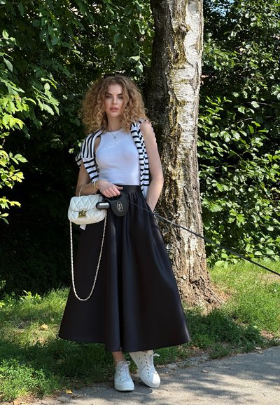 Falda midi negra con textura lisa, combinada con una camiseta blanca sin mangas y un chaleco a rayas. Los accesorios incluyen un bolso blanco acolchado y zapatillas blancas.