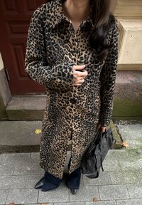 Kabát s leopardím vzorom z mäkkej tkaniny s zapínaním na gombíky vpredu, s dlhými rukávmi a voľným strihom, doplnený čiernou taškou a zvonovými džínsami.
