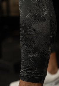 Leggings de compressão com padrão preto e cinza, apresentando uma textura suave, com um discreto logótipo da Nike e detalhes em costura flatlock.
