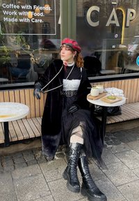 Μαύρο ψεύτικο γούνα παλτό πάνω από λευκό κορσέ, με στρωμένο τούλινη φούστα, σχέδιο καλσόν και μαύρες μπότες με κορδόνια. Τα αξεσουάρ περιλαμβάνουν ένα κόκκινο καρό μπερέ.