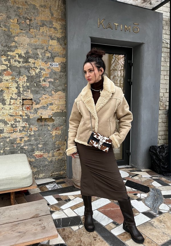 Bēdīgo aitu kažociņu ar platām apkaklītēm, kombinēts ar brūnu pieguļošu midi kleitu un brūnām augstām zābakiem līdz ceļiem. Somiņa ar govs rakstu.