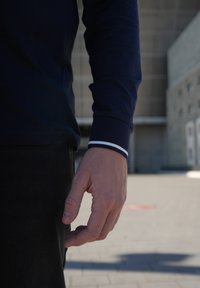 Marineblå langærmet skjorte med hvide striber ved manchetterne, sammen med mørke bukser. Hånden er afslappet og griber let.