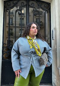 Grey, textured button-up top with a drawstring waist, teamed with green trousers. Accessories include a patterned scarf and a small leopard-print bag.