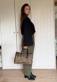 Tasje met luipaardprint en zwarte handvaten, gedragen met een oversized zwart top en olijfgroene broek, gecombineerd met zwarte haklaarzen.