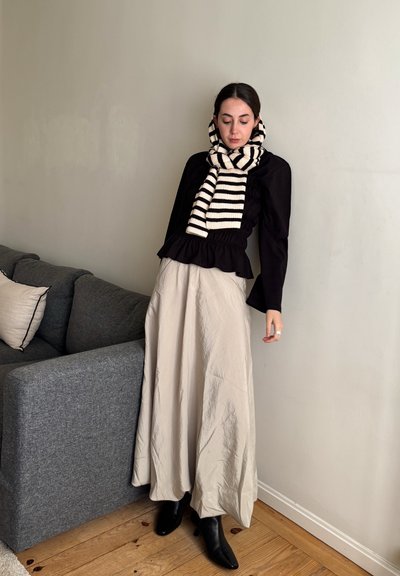 Top negro de manga larga con cintura fruncida, falda crema y botas negras con tacón; bufanda de punto a rayas, textura lisa, patrones mínimos.