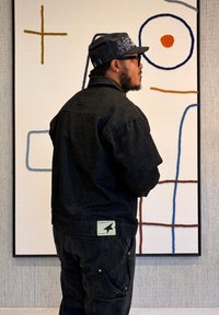 Veste en denim noir et pantalon assorti, avec une finition texturée. La veste présente une étiquette à l'arrière avec un logo. Art abstrait en arrière-plan.