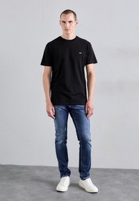 Černé bavlněné tričko s kulatým výstřihem, spárované s popraskanými modrými džíny a bílými teniskami. Jednoduchý design, přiléhavý silueta.