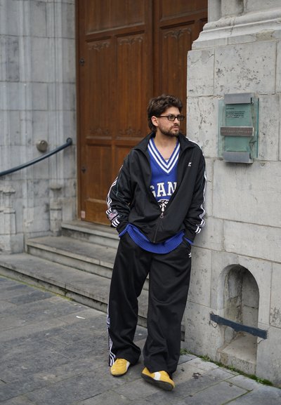 Chaqueta negra con cremallera, camiseta azul con acentos blancos, pantalones negros holgados y zapatos amarillos. Materiales texturizados, estilo deportivo, entorno urbano.