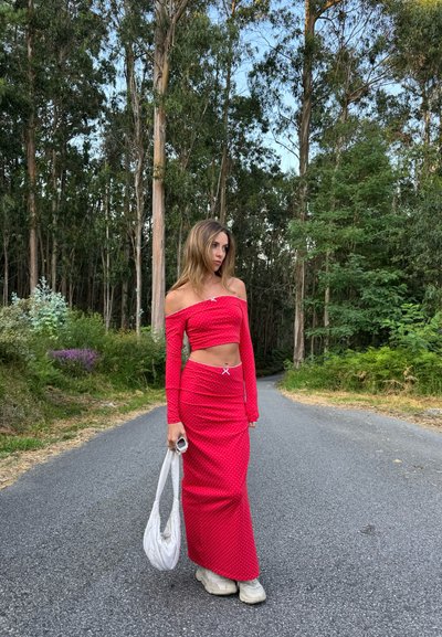 Top corto rojo sin mangas y falda larga a juego con lunares blancos, que cuenta con una abertura lateral y detalles en blanco. Combinado con zapatillas blancas.