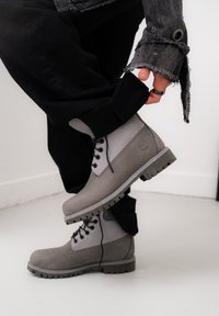 Gray ankle boots with a textured finish, featuring a contrasting lighter grey side, black laces, and a rugged rubber sole.