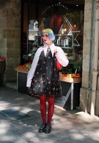 Robe noire avec un imprimé de fraises rouges, jupe superposée, chemise blanche en dessous. Collants rouges et chaussures noires épaisses. Cheveux colorés et accessoires.