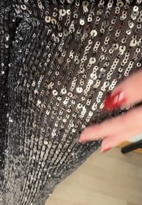 Zwart paillettenstof met zilveren cirkelvormige pailletten gerangschikt in verticale lijnen; gladde textuur met fonkelende accenten die de reflecterende kwaliteit benadrukken.