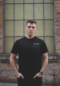 Melns īsām piedurknēm T-krekls ar teksturētu kabatu, kurai ir ģeometrisks raksts, ar zīmolu "KARL LAGERFELD" baltā krāsā.