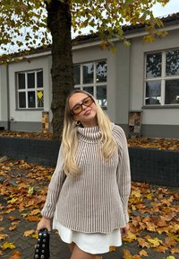 Beige en witte gestreepte trui met een col, gedragen over een witte jurk, gecombineerd met ronde zonnebril en een zwarte tas met studs.