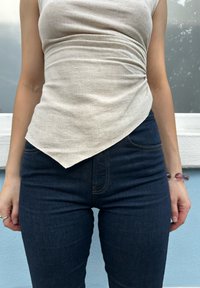 Κρέμας χρώματος, υφασμάτινη αμάνικη μπλούζα με διαγώνιο στρίφωμα, σε συνδυασμό με σκούρα τζιν skinny παντελόνια που διαθέτουν αντίθετη ραφή.