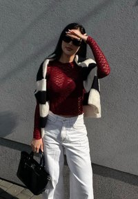 Κόκκινη δανδελένια μπλούζα με μακριά μανίκια, λευκά τσιμωμένα ψηλά τζιν με φαρδιά πόδια, μαύρη πλισέ τσάντα και έναν μαύρο-άσπρο patterned σ scarf ριγμένο στους ώμους.