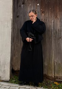 Zwarte wollen jas met grote revers over een lange zwarte jurk. De persoon houdt een kleine zwarte tas vast, met een gestructureerde houten achtergrond.